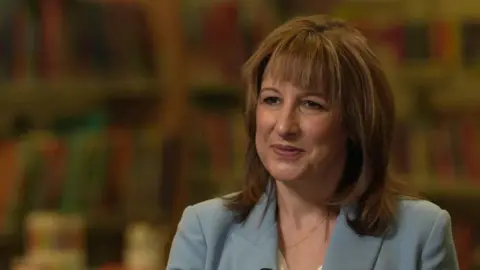 Chancellor Rachel Reeves, sitting down being interviewed, wearing a light blue suit jacket