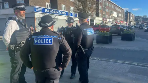 Four members of the Metropolitan Police stand at one end of Farnham Road in Harold Hill. 