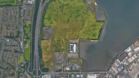 Google Maps A satellite image of North Belfast. To the left can be seen the residential areas of the shore road, and to the right, the harbour estate with commercial buildings and port space. In the middle is the grass of Giant's Park with the motorway alongside it. 