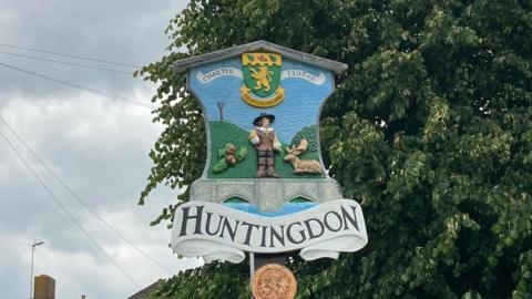 Sign of Huntingdon with acorns, deer a man and the words Charter 1205 written above 