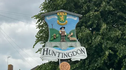 BBC Sign of Huntingdon with acorns, deer a man and the words Charter 1205 written above 