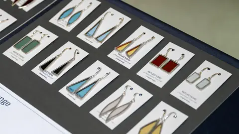 Manchester City Council Different coloured and shaped glass dangly earrings displayed on a board.