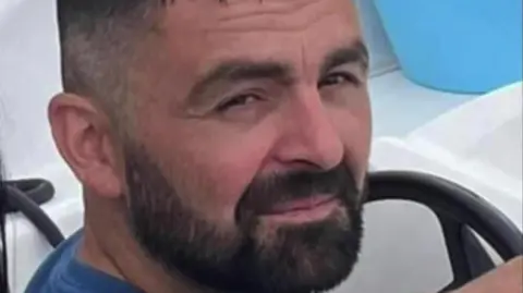 Supplied Michael Barnard is wearing a dark blue T shirt. He has short, dark hair and a beard and moustache. He looks like he's behind the wheel of a white motor boat - the wheel and white dashboard are just visible.