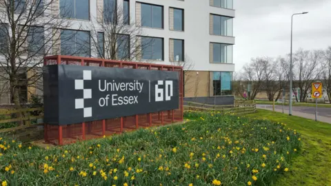 University of Essex A black sign that reads University of Essex and a building behind 