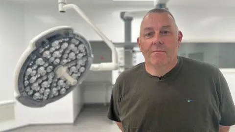 BBC/ Mark Denten Patient Jason Sykes, wearing a khaki t-shirt, stands in the new operating theatre.