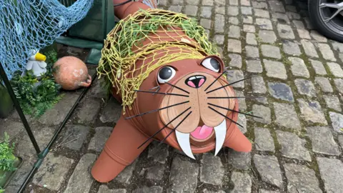 BBC/Amber Gash A walrus with a smiling face and large tusks has been made using brown flower pots. It is laid on a cobbled path and surrounded by fishing nets.