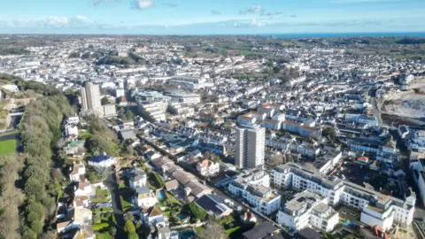 An aerial view of St Helier with a plethora of houses and buildings with the sea and sky further afield.
