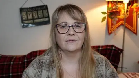 Qays Najm/BBC Mel Collins looks expressionless at the camera. She has long blonde hair with a fringe. She wears glasses along with a green coloured shirt. 