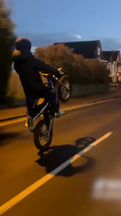 Night-time shot of an anonymous electric bike rider doing a wheelie on a road 