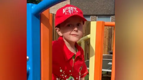 Kev Pitcher Benny Pitcher stands at the top of a small orange and yellow park slide. 