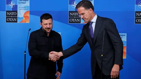 Omar Havana/Getty Images The Ukrainian leader on the left wearing black shakes hands with the taller Dutch Nato Secretary General Mark Rutte against a blue background