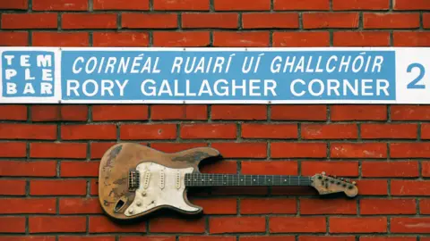 Getty Images Guitar and blue and white Rory Gallagher Corner street sign on red brick wall in Dublin's Temple Bar area