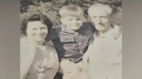 Contributed A black and white image of a man and a woman with a young boy in the middle of them. They are all smiling at the camera. 