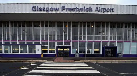 Getty Images The entrance to a large airport building, with the view coming from across the street. The sign says Glasgow Prestwick Airport