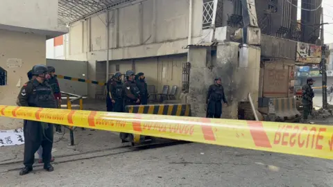 BBC Part of the Federal Constabulary headquarters in Peshawar cordoned off with yellow tape after a suicide bomb attack. Security officers armed with guns are seen on site