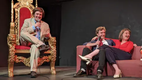 Dave Natriss A man dressed as Terry Wogan, sat in a big golden thrown, interviews a man and woman dressed as Tony and Cherie Blair.