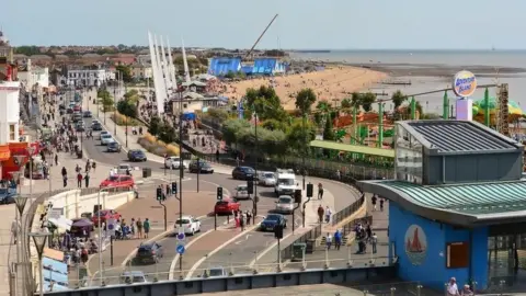 A bustling Southend-on-Sea seafront, with the beach and theme park in the background. A busy road is in the foreground.