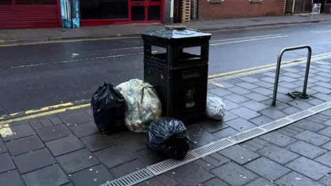 Four general waste bags dumped next to a black public litter bin on Cowbridge Road East in Canton.