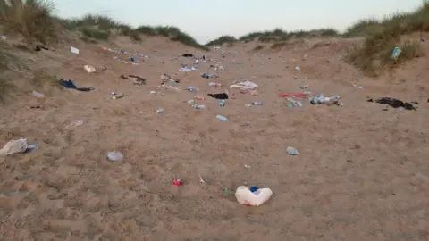 Paul Granger A sand dune is littered with plastic bottles, cans and other discarded rubbish.
