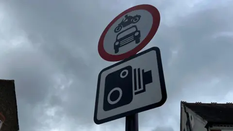 Circular red sign with car and bike inside and square camera sign just below