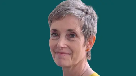 Hertfordshire County Council Sarah Perman with short light brown hair smiling at the camera wearing a yellow top against a dark background
