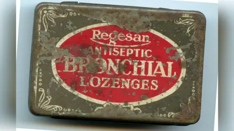 A old, rusted tin of lozenges. It has a red sticker on it. 
