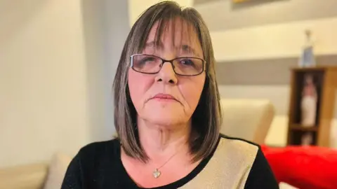 Janette Binnie looking at camera, she is wearing a black and beige top and a necklace.