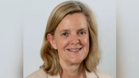 A headshot of Tandridge District Council leader Catherine Sayer, who has shoulder length fair hair and is wearing a beige jacket. She is only visible from the shoulders up. 