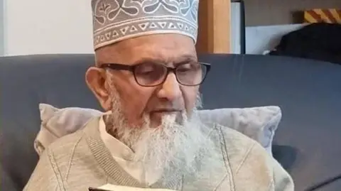 A head and shoulder photo of Qari Ismaeel Khandia looking down. He is wearing glasses and has a grey beard 