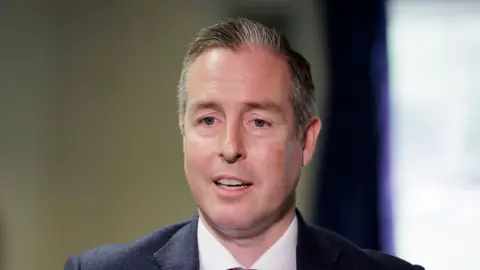 PA Media A man with short grey hair is pictured talking to someone off camera. He is dressed in a navy suit jacket, a white shirt, and a burgundy patterned tie. 