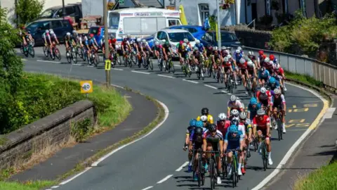 Getty Images A peloton of cyclists cycling round a corner on a Welsh road over a small stone bridge