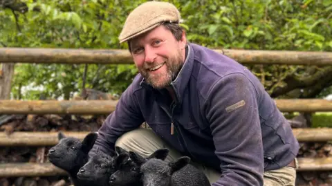 Farmer Tom Martin cuddles four black lambs