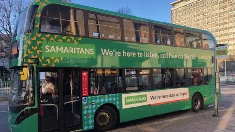 Samaritans A photo of the green bus parked in Plymouth city centre. It is green and has the charity's logo on the side of it.