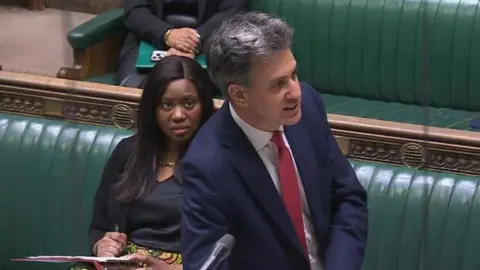 Parliament TV Picture of Ed Miliband speaking on the green benches of the House of Commons. 