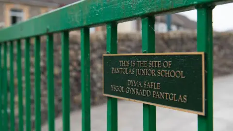 Getty Images A close-up image of green railings and a plaque which reads 'This is the site of Pantglas Junior School' in English and Welsh. In the background, blurred, is a stone wall. 