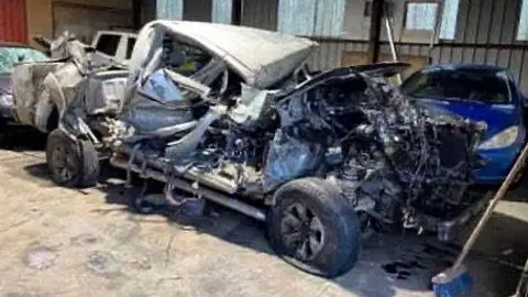 Gavin Smith A totally demolished grey pick up truck. The bonnet is smash off and the roof is crushed. The vehicle is in a car shop with other cars in the background. 