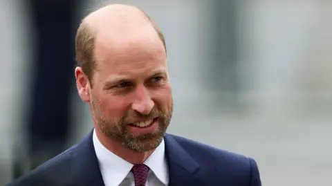 Reuters Mid-shot of Prince William wearing a bluish  suit, achromatic  garment  with bluish  and reddish  tie.