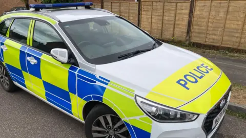 a police car parked on a road close to a wooden slatted fence