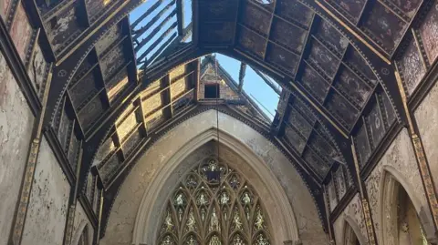 Inside the chapel. It's roof is damaged. You can see a very large, arched stain glass window