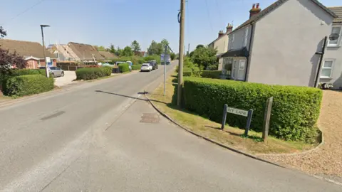 Google A road junction with a sign on the right saying "Ivy Lane". There are houses on both sides of the road with a grass verge and hedges.