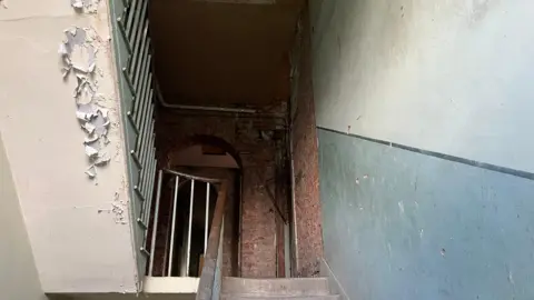 Interior staircase showing bare brick and peeling pain