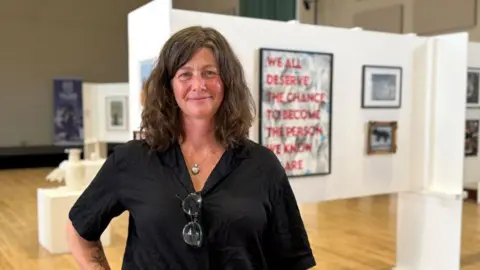 Keele University A woman standing in an art gallery, with artworks displayed on exhibition panels behind her.