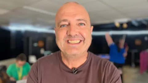 Fraser Howat looks into the camera - he is smiling and is wearing a brown t-shirt.
