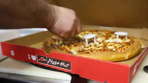 Getty Images A person reaches into a pizza box and cuts a pizza
