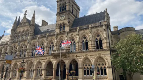 The exterior of Northampton's Guildhall bulding with a union jack and Armed Forces Day flag being flown.