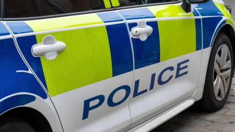 A white, yellow and blue police car parked on a road.