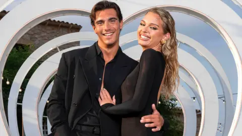 ITV/Shutterstock Lorenzo Alessi and Julia Majchrzak pose in front of a heart-shaped cut-out. Lorenzo is wearing a black suit and Julia a black dress. 