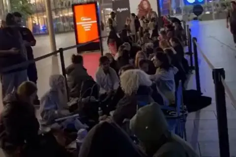 Ashillous_25 Instagram/TikTok A line of shoppers sat down on the floor between barriers