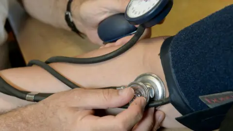 A hand holds a stethoscope on a person's arm.