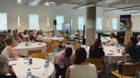 BBC/NATHAN TURVEY Tracey Brabin on the left addressing people sat at round tables at a special event at Bradford College.